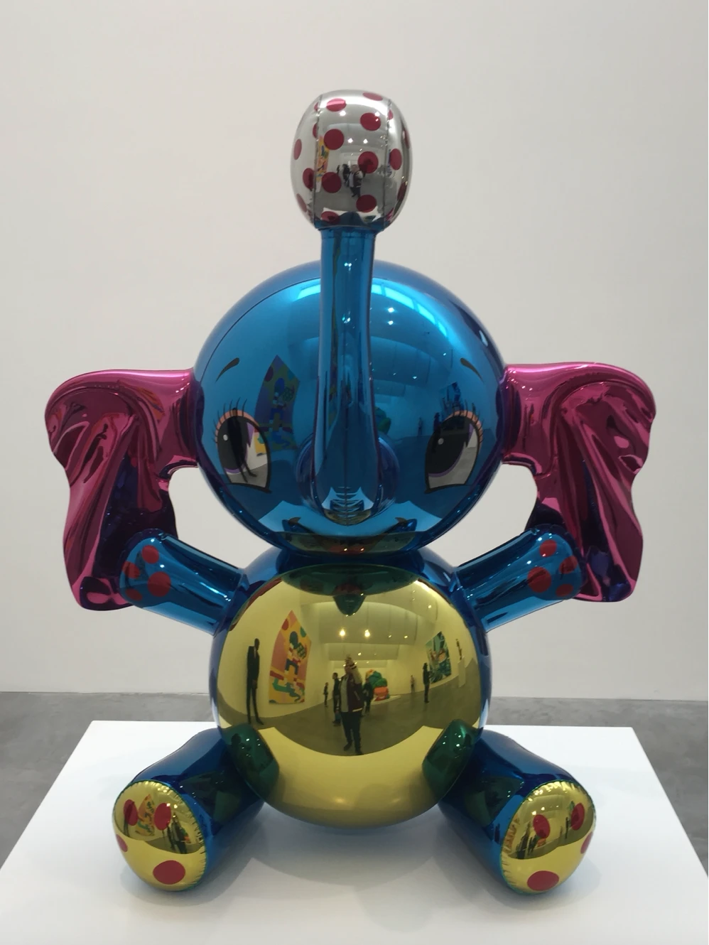 Reflective blue elephant sculpture with pink ears and a gold belly